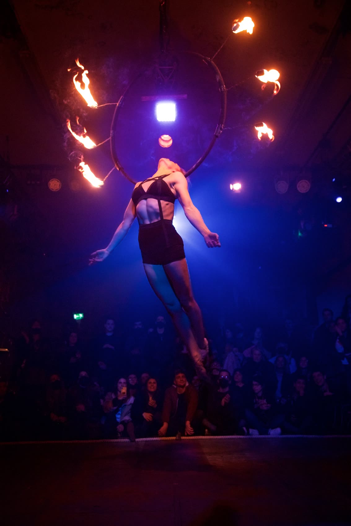 An aerial performer suspended inside a fire-lit hoop above a watching crowd