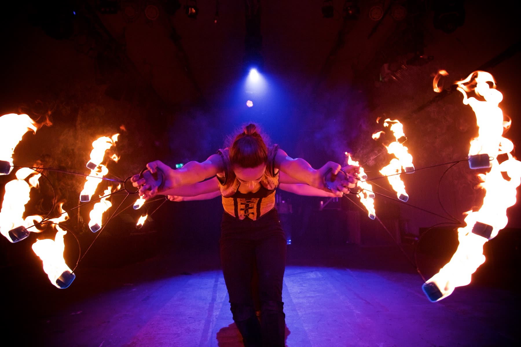 A fire performer spinning lit fans under magenta stage light